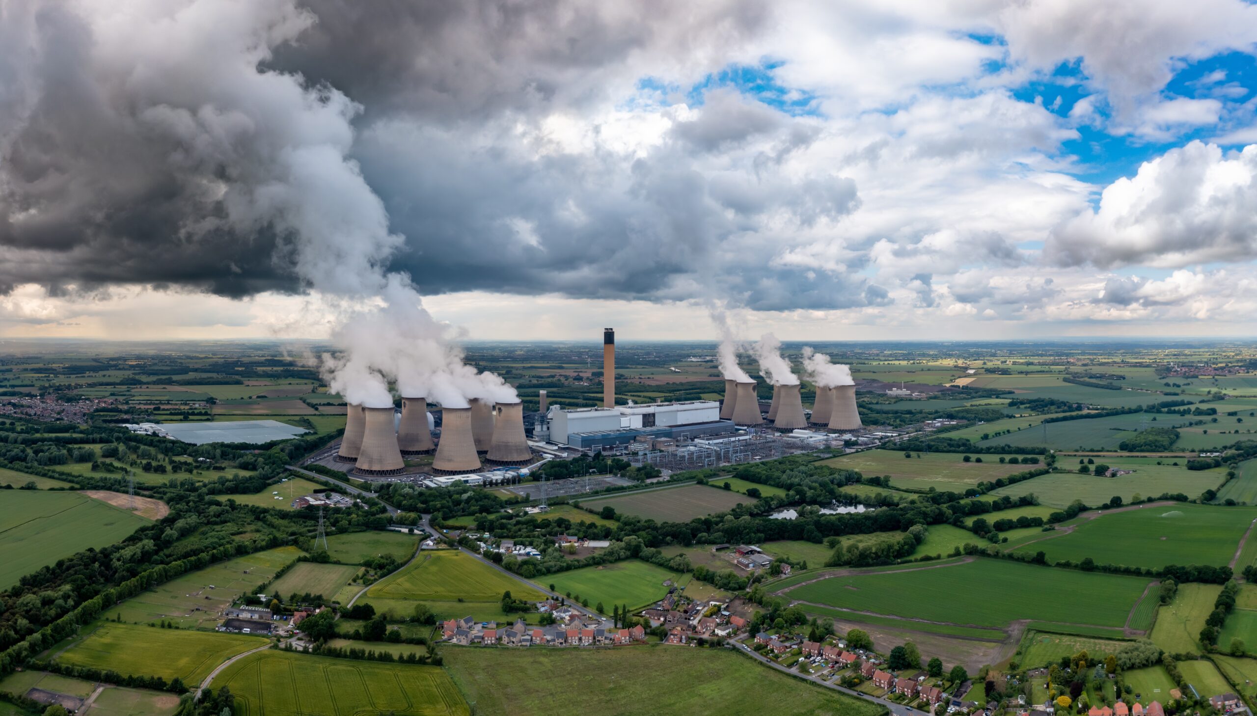 a view across fields of a power station with large chimneys and smoke billowing into the sky