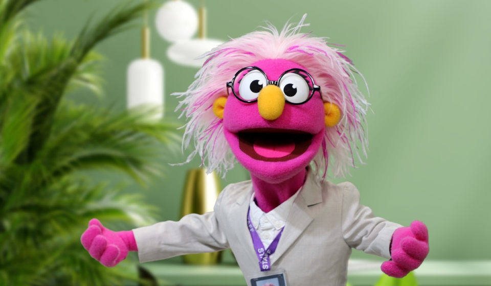 case study - wellcome connie1200x700 a bright pink puppet with floppy feathery hair and a yellow nose - arms wide open in an office setting